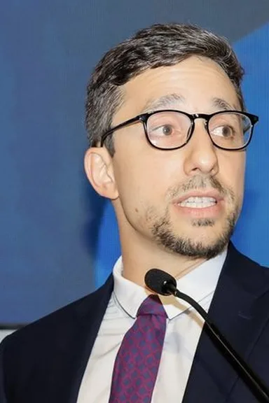 Gianluca Venturi in a suit, a microphone in front of him